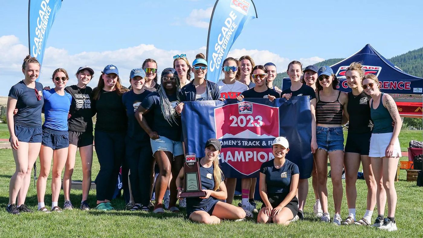 A college women’s track and field team with their conference championship banner and trophy