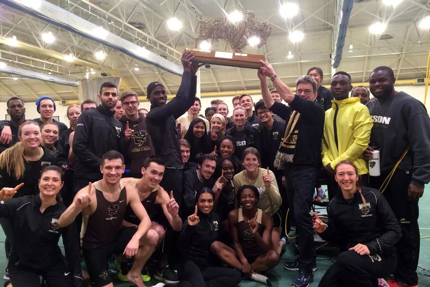 A college track and field team holding up a championship trophy at an indoor meet